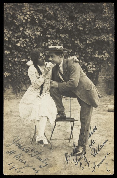 Download the full-sized image of Two actors, one in drag, pose on garden furniture. Photographic postcard, 1918.