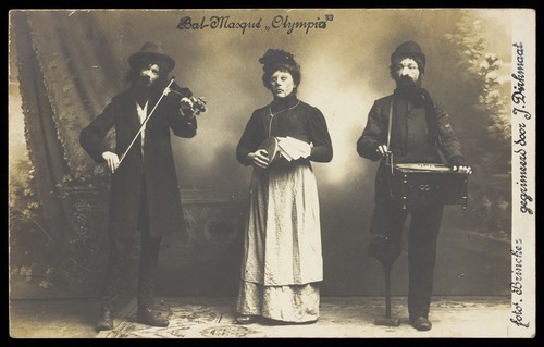 Download the full-sized image of Three musicians, one in drag, in bizarre masks for an "Olympia" masked ball. Photographic postcard by Brincker, 191-.