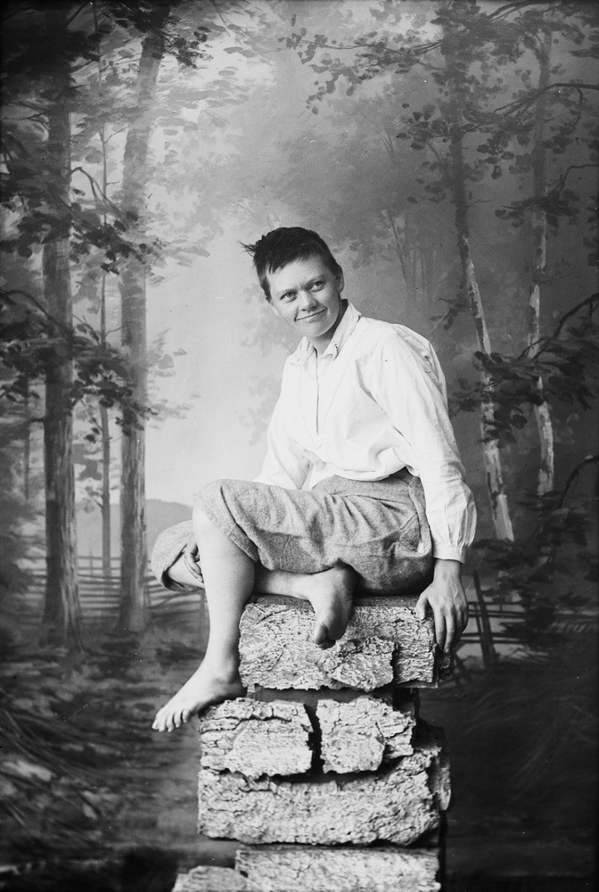 Download the full-sized image of Marie Høeg Sits on a Pile of Rocks in Traditional Men's Attire
