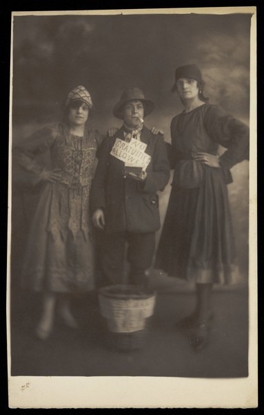 Download the full-sized image of Three actors in drag, posing in a variety of costumes; in front of a basket on the floor. Photographic postcard, 191-.