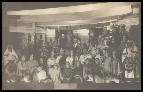 Download the full-sized image of Amateur actors, some in drag, pose on a crowded stage. Photographic postcard, 191-.