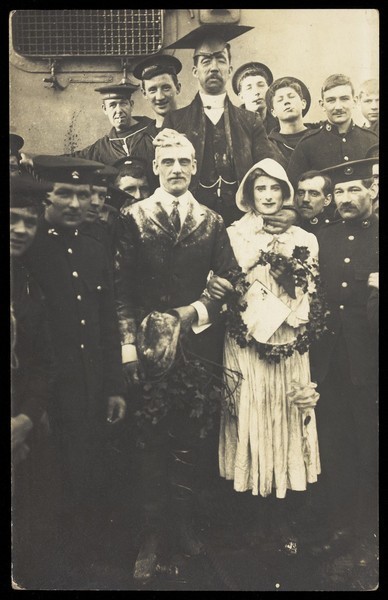 Download the full-sized image of Sailors on H.M.S Dominion, one in bridal drag, conduct a mock wedding on Christmas Day. Photographic postcard, 1915.