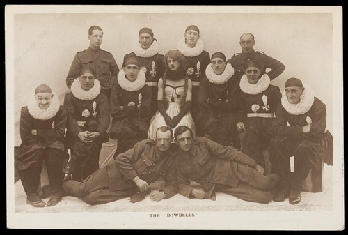 Download the full-sized image of Amateur actors, one in drag, known as "The Bowbells"; posing for a group portrait. Photographic postcard, 191-.