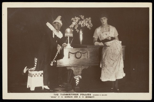 Download the full-sized image of Two British prisoners of war, one in drag, posing for "The Timbertown Follies", at a prisoner of war camp in Groningen. Photographic postcard, 191-.