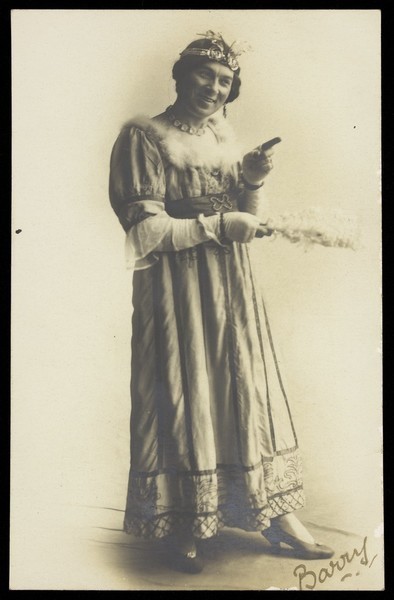 Download the full-sized image of A man in drag, holding a feather, performing in the play 'A country girl'. Photographic postcard, 1920.