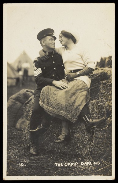 Download the full-sized image of Two soldiers embracing on a bale of hay, one in drag. Photographic postcard, 191-.