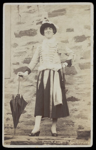 Download the full-sized image of A man in drag posing with an umbrella, with a 3rd prize label attached to his shoulder. Photographic postcard, 192-.