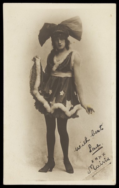 Download the full-sized image of A man in drag poses wearing a short dress and large bow tie-shaped head garment. Photographic postcard, 192-.