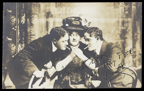 Download the full-sized image of Three actors (George, Joey and Jock Preston), one in drag, pose lighting cigarettes. Photographic postcard, 1910.