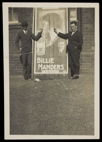 Download the full-sized image of Two members of the Quaintesques pose in front of a poster advertising Billie Manders. Photograph, 192-.
