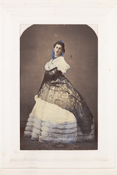 Download the full-sized image of A man in drag poses wearing an elaborate dress. Coloured photograph, 189-.