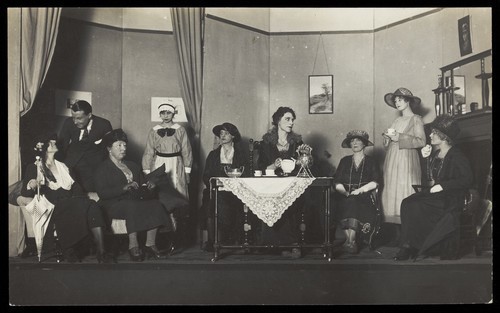 Download the full-sized image of Amateur actors, some in drag, are having tea on stage. Photographic postcard, 192-.