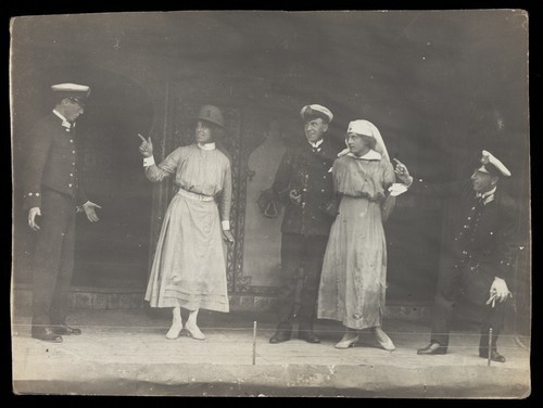 Download the full-sized image of Sailors, some in drag, performing a scene on stage. Photographic postcard, 191-.