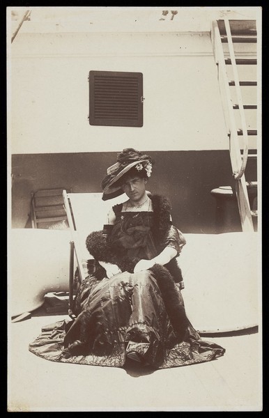 Download the full-sized image of A sailor in drag sits on the deck of a ship in bright sunlight. Photographic postcard, 191-.