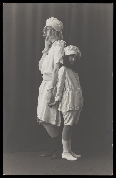 Download the full-sized image of Ralph Mellor in drag and a young actress stand back-to-back on stage. Photographic postcard by L.S. Langfier, 192-.