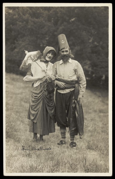 Download the full-sized image of Harry Smallwood and another man stand in a field, one in drag and the other wearing Turkish inspired costume. Photographic postcard, 1925-.