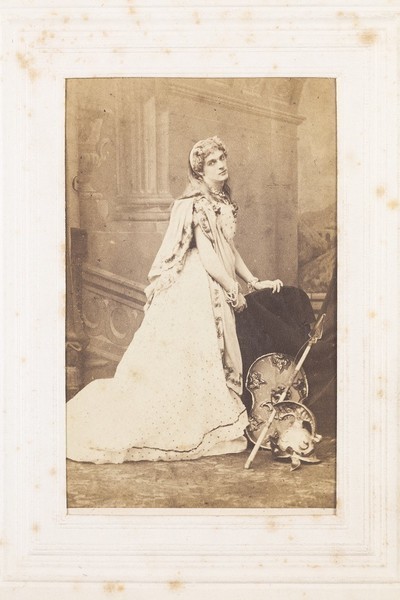 Download the full-sized image of A man in drag posing in bridal costume next to Centurion-style props. Photograph, 189-.