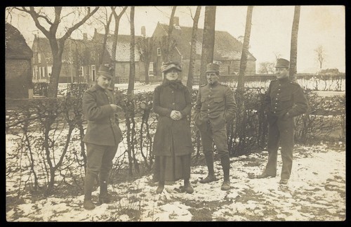 Download the full-sized image of Four Dutch servicemen, one in drag, standing on snowy ground near residential property. Photographic postcard, ca. 1910.