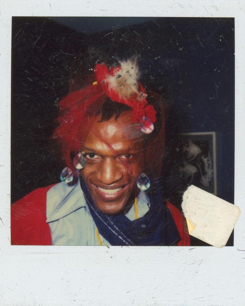Download the full-sized image of A Photograph of Marsha P. Johnson Smiling at the Camera Wearing a Red Mesh Headpiece with Large Gems