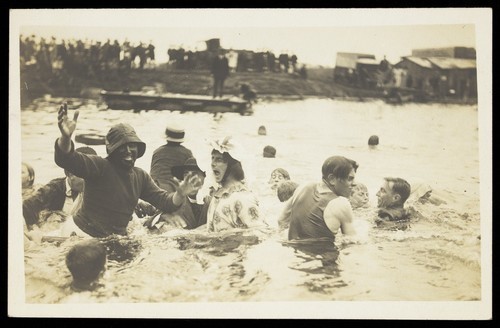 Download the full-sized image of People, one in drag, thrashing around in a river. Photographic postcard, ca. 1920.