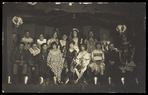 Download the full-sized image of An ensemble cast of British soldiers, some in drag, pose on stage. Photographic postcard, 1919.