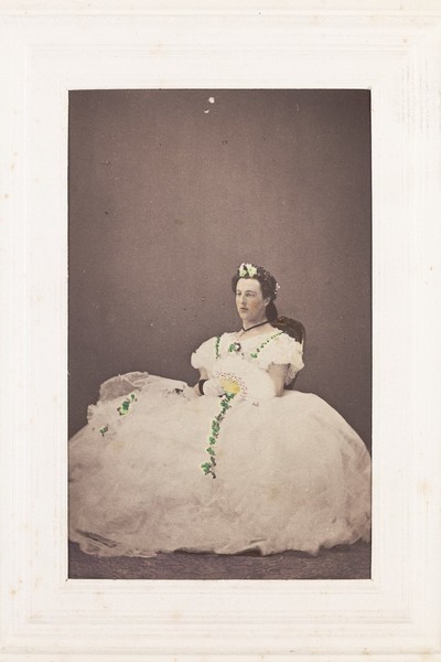 Download the full-sized image of A man in drag is sitting down wearing a large white dress. Photograph, 189-.
