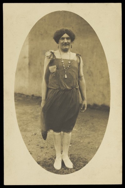 Download the full-sized image of An amateur actor in drag, wearing a flapper dress and white footwear. Photographic postcard, 1925-1928.